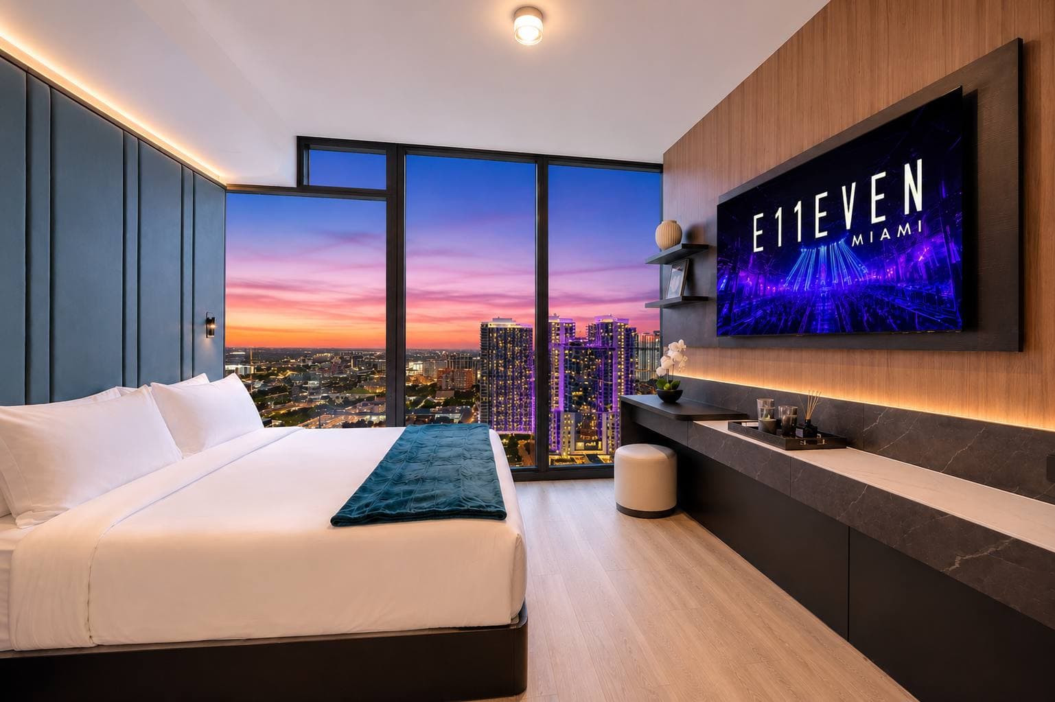 Bed beside city-view windows at dusk.