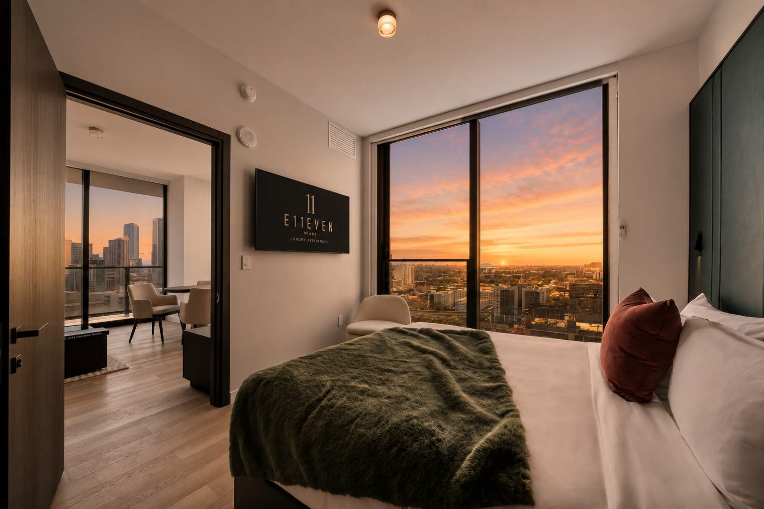 Bed beside city-view windows at dusk.