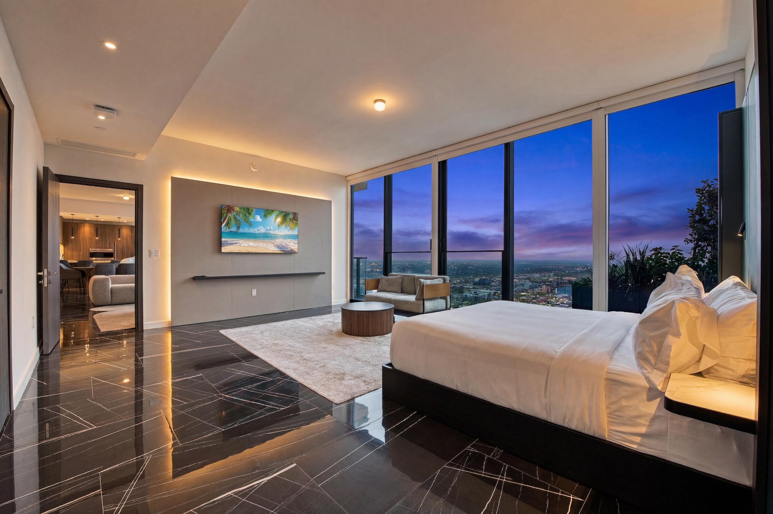 Spacious bedroom overlooking city lights at dusk.