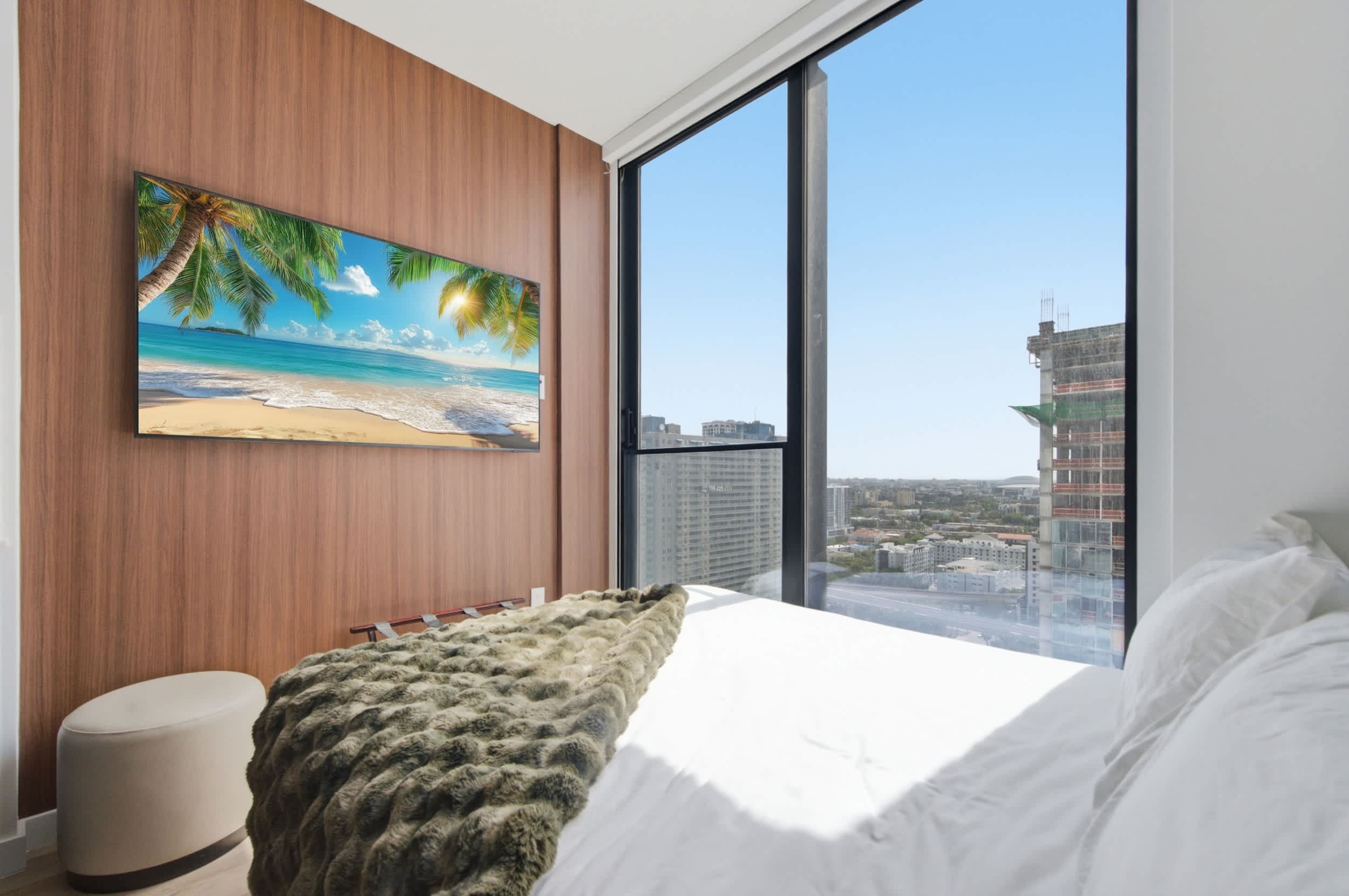 Bed beside a television and city-view window.