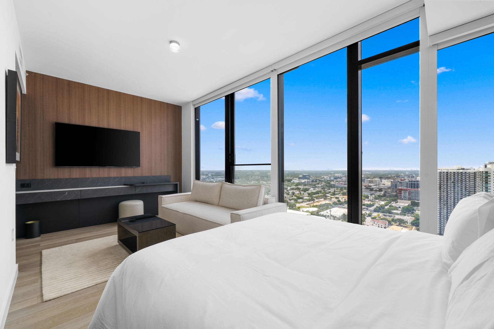 Bed beside floor-to-ceiling city-view windows.