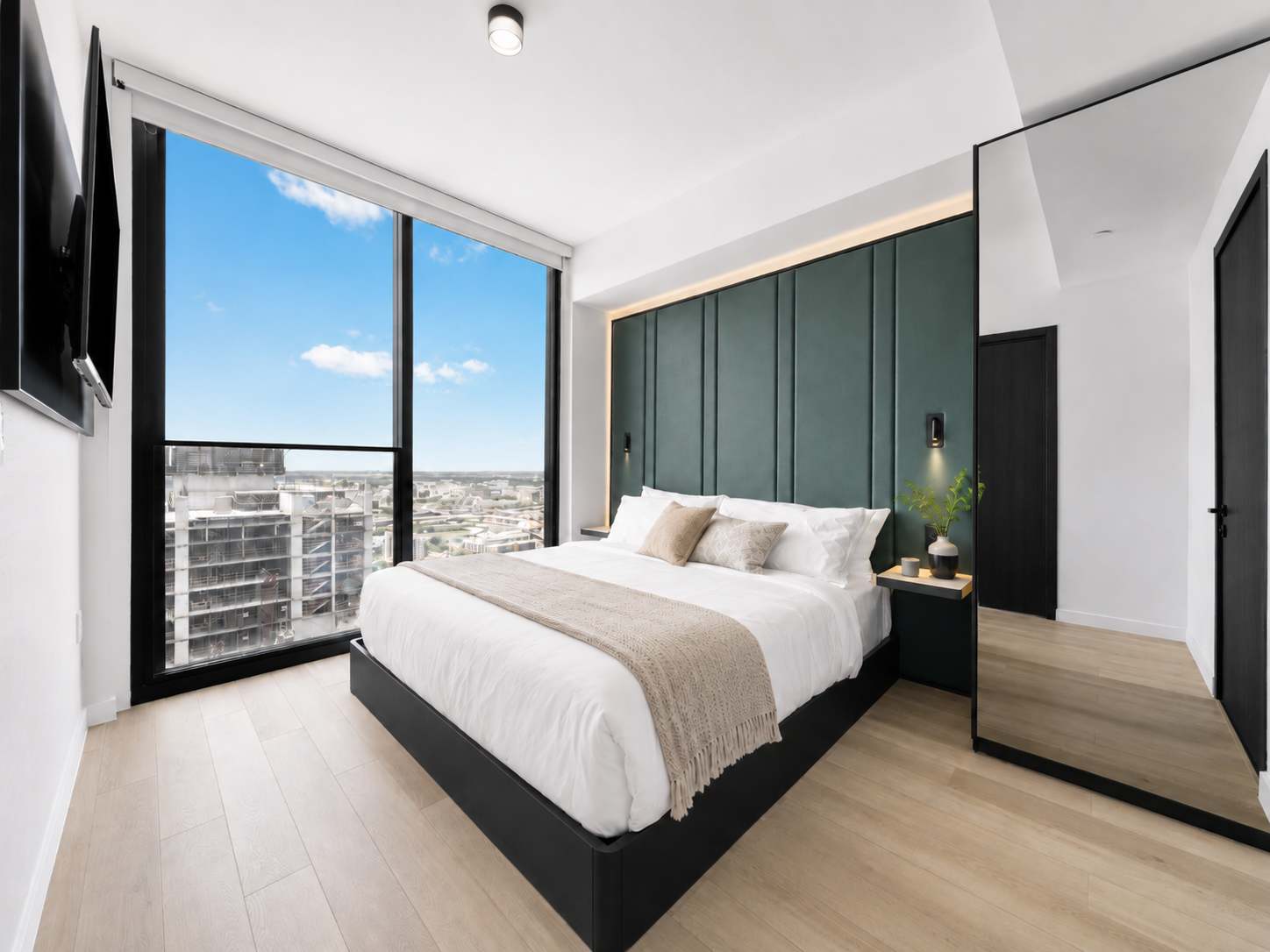 Bed beside floor-to-ceiling city-view windows.