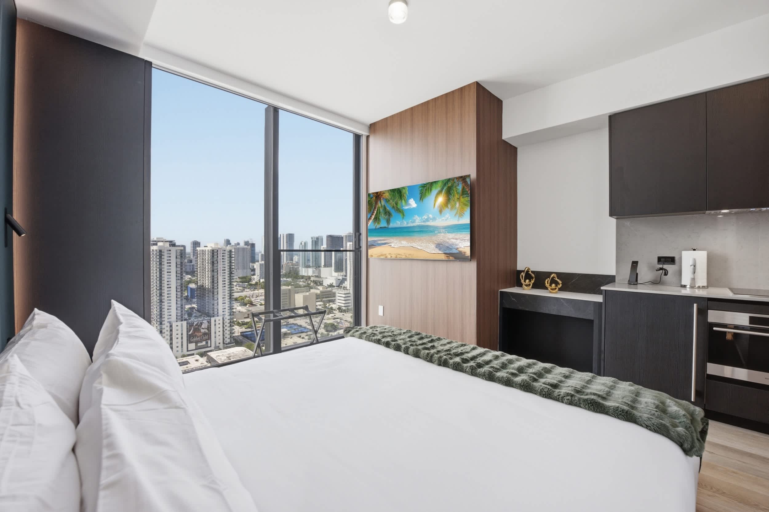 Bed beside a compact kitchen and city views.