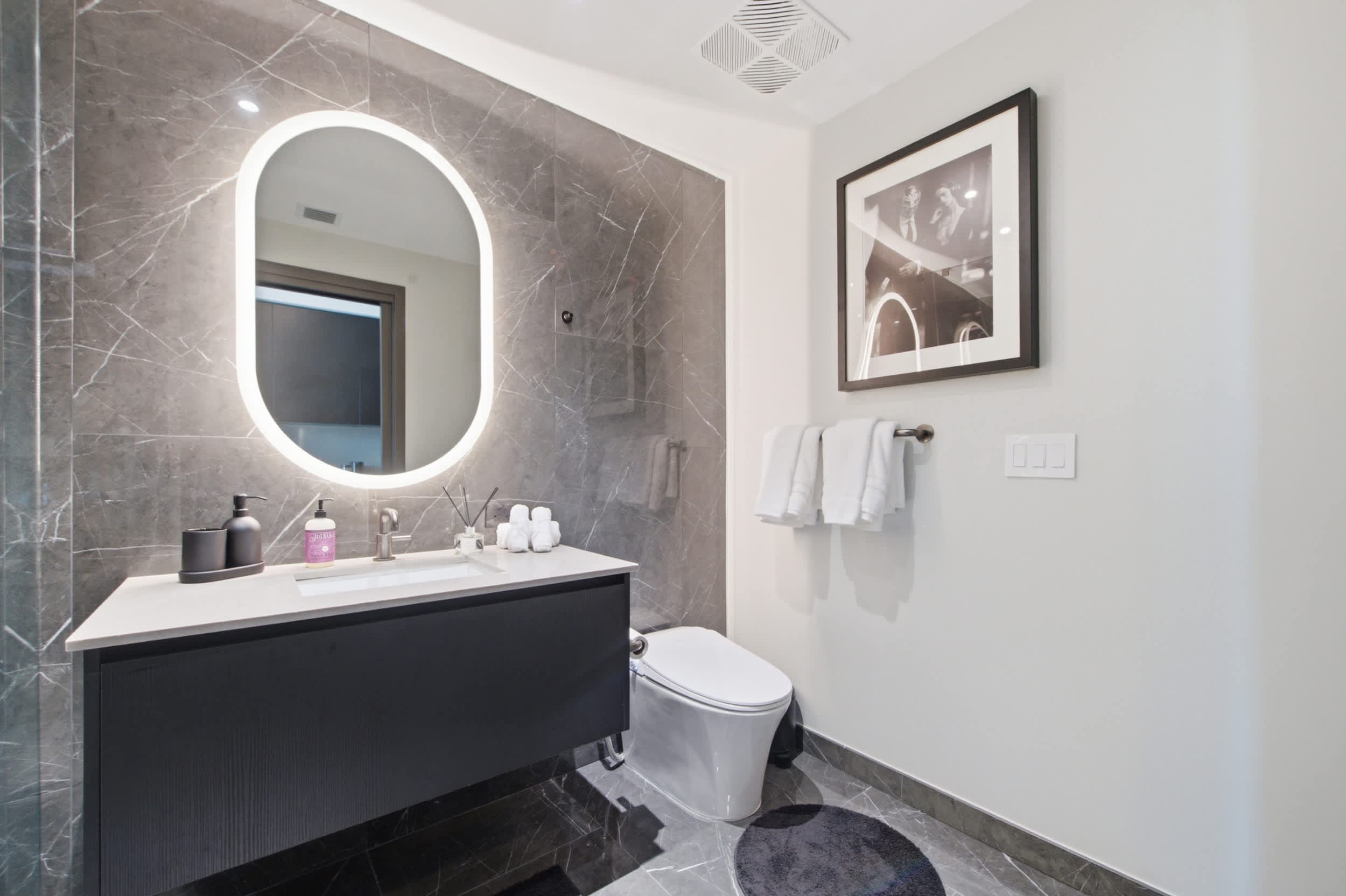 Bathroom vanity beneath an illuminated oval mirror.