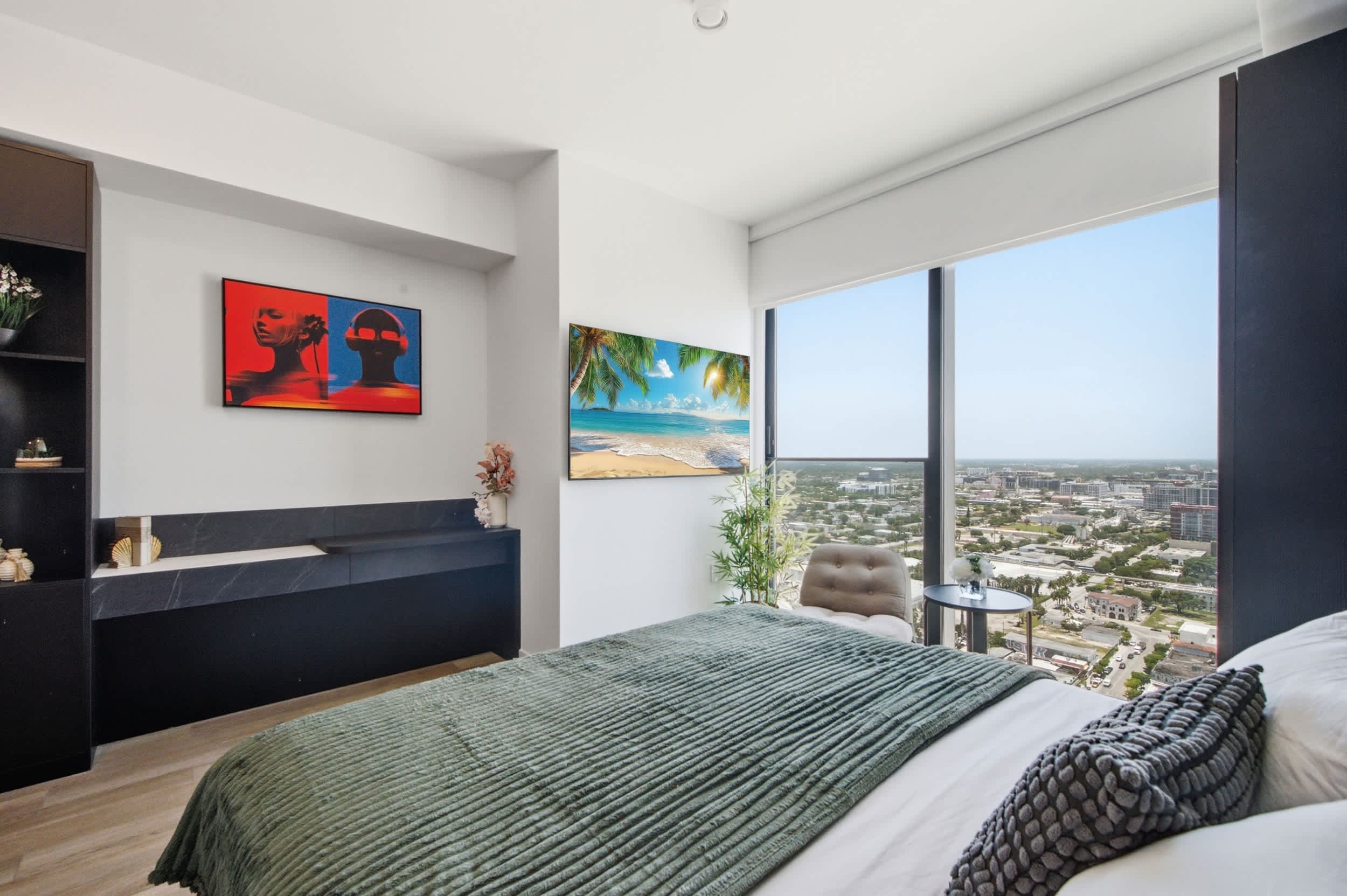 Bed facing a television beside city-view windows.