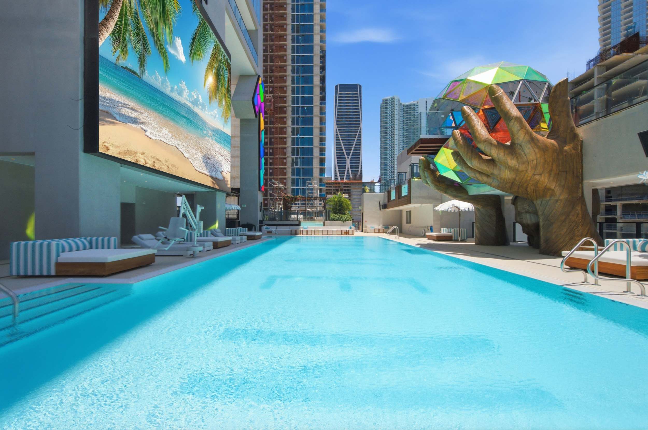 Swimming pool beside a sculpture and large screen.