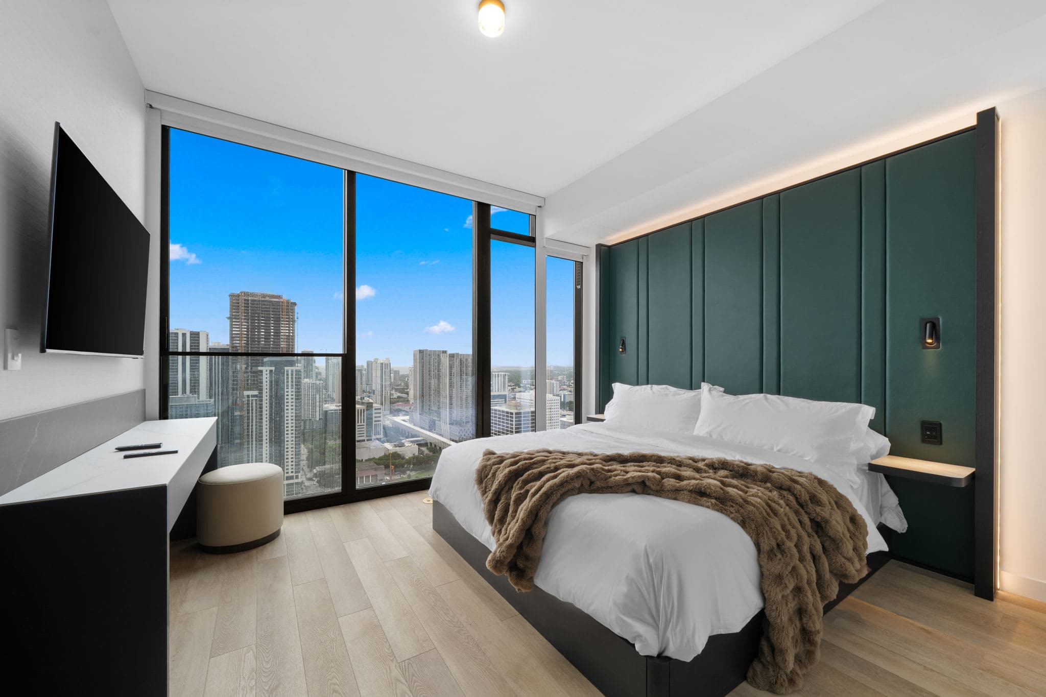 Bed beside large city-view windows.