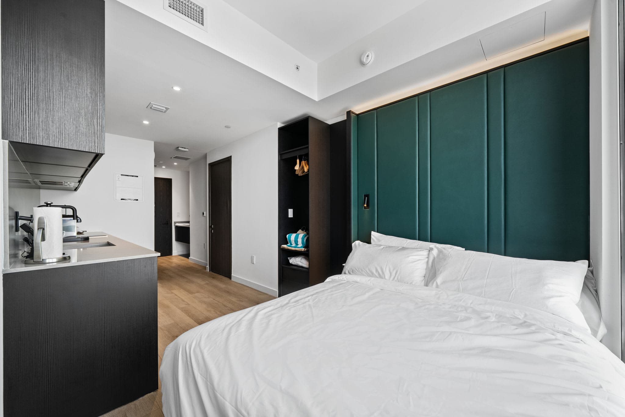 Bed beside a green headboard and compact kitchen.