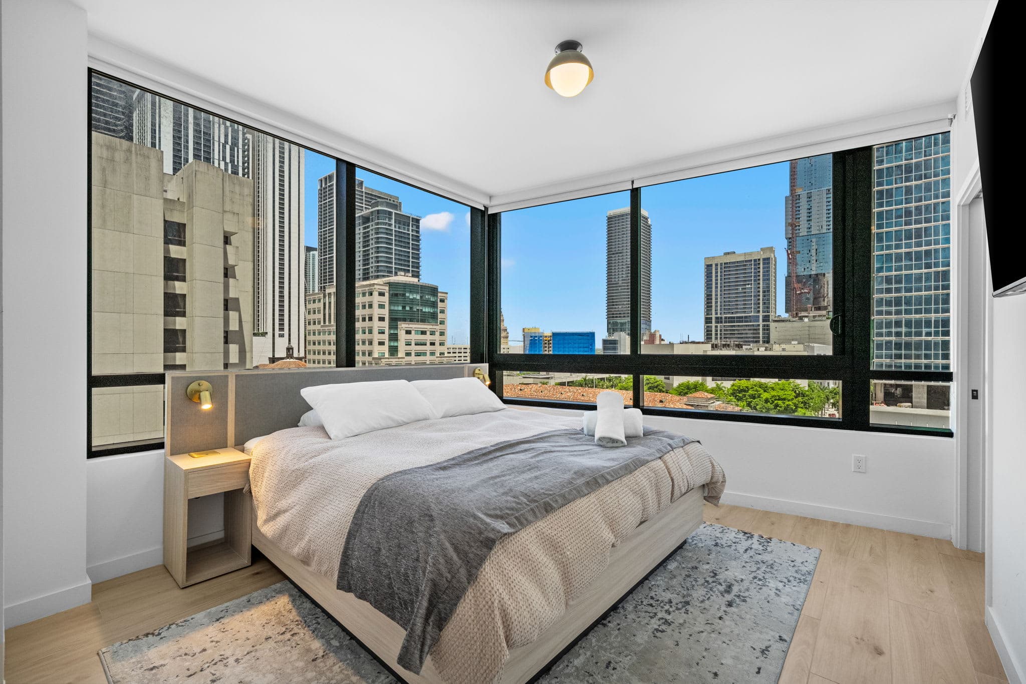 Bed beside large city-view windows.