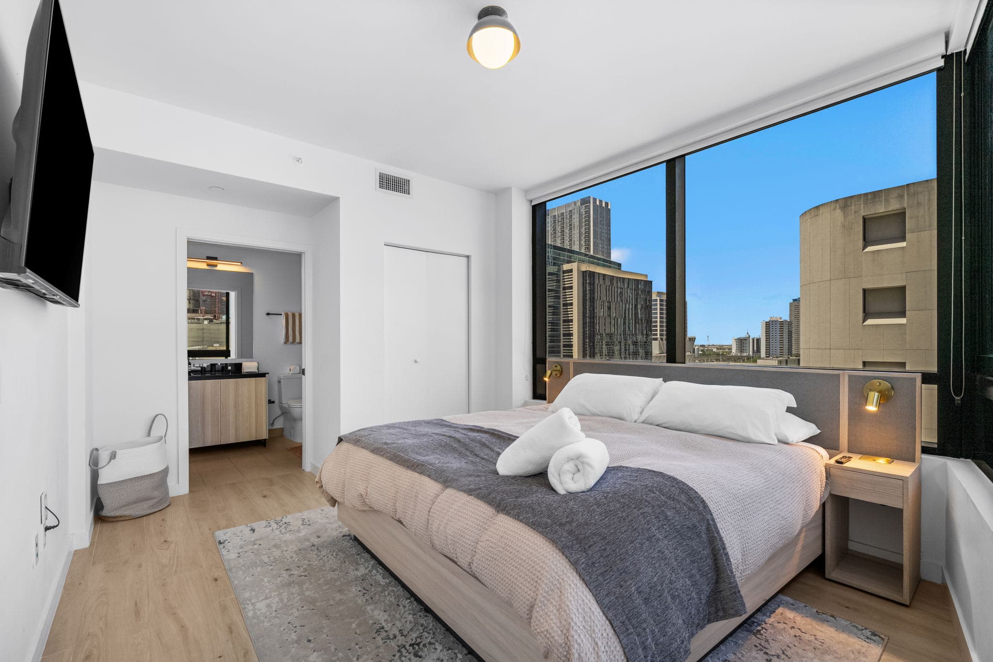 Bed beside large city-view windows.