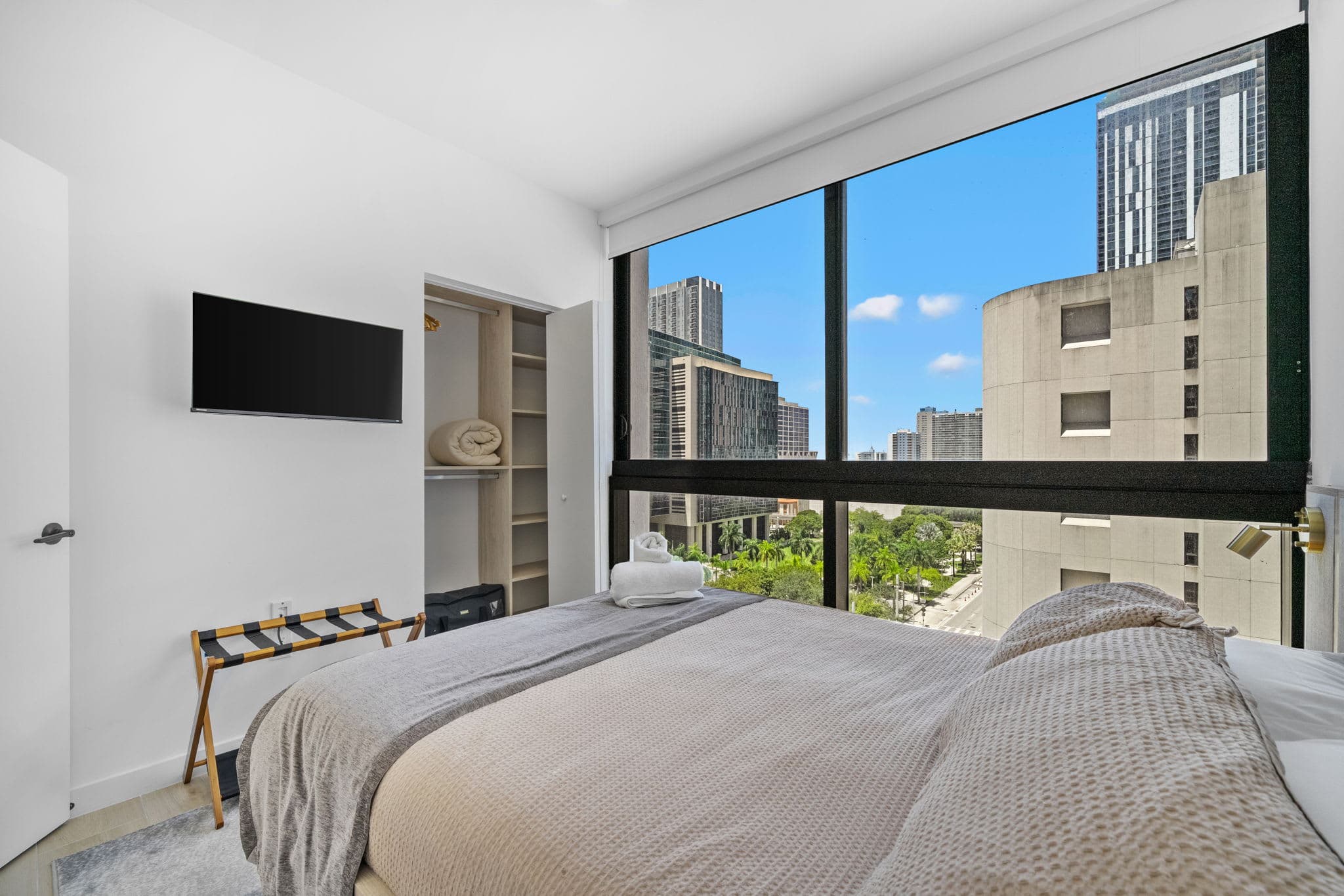 Bed beside large city-view windows.