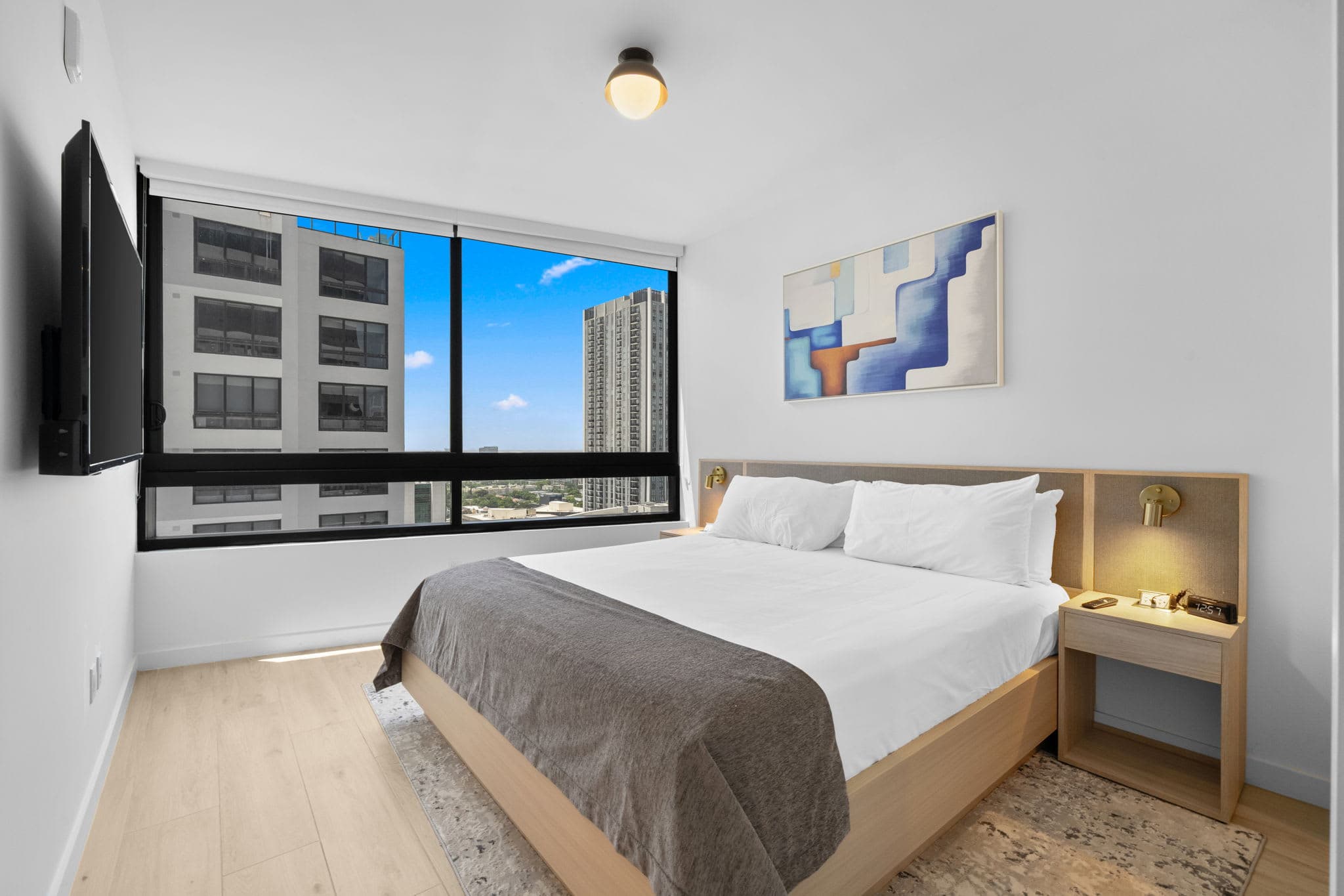 Bed beside large city-view windows.